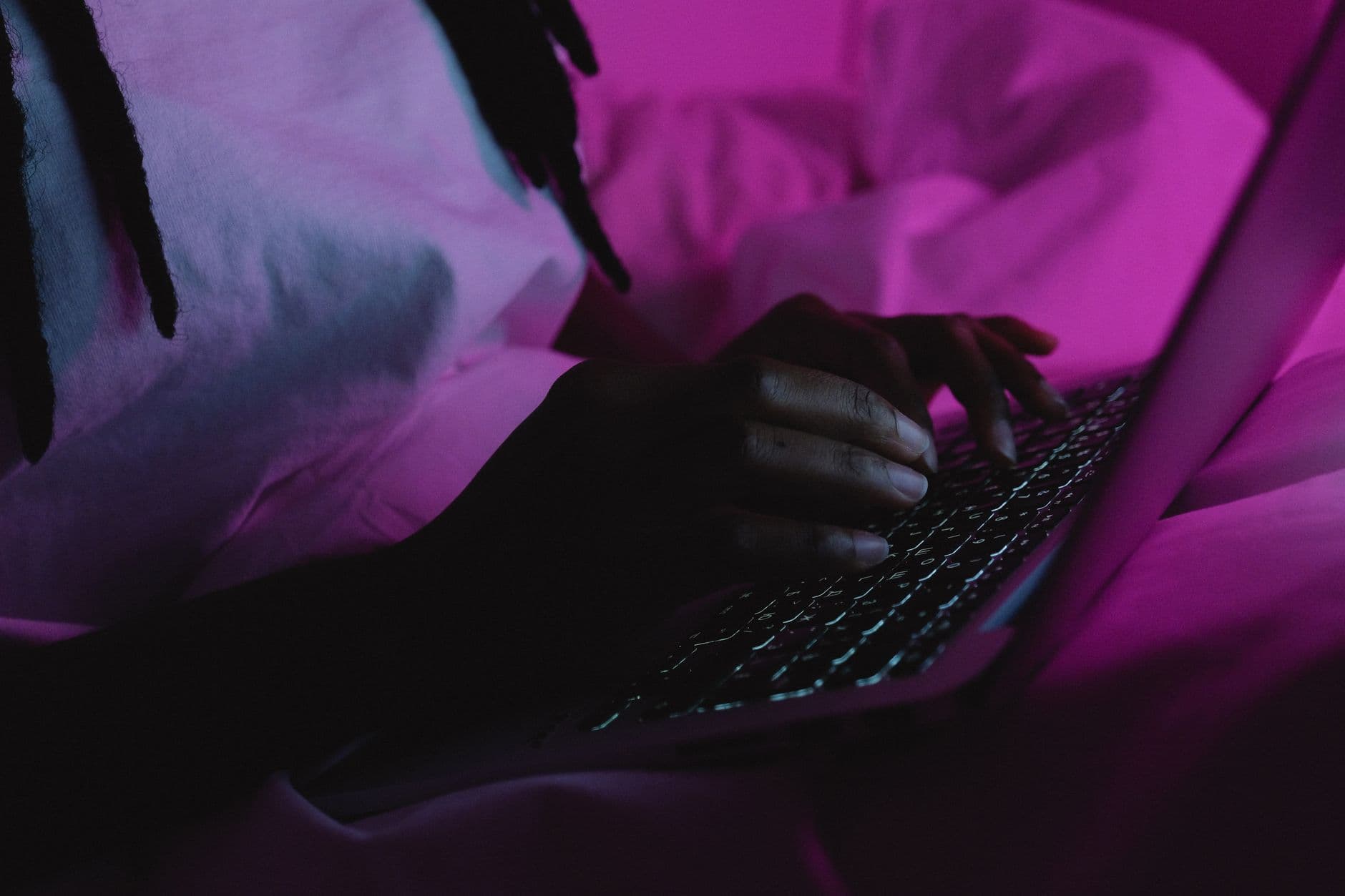 A person typing on a laptop under vibrant pink lighting, creating a dramatic atmosphere.