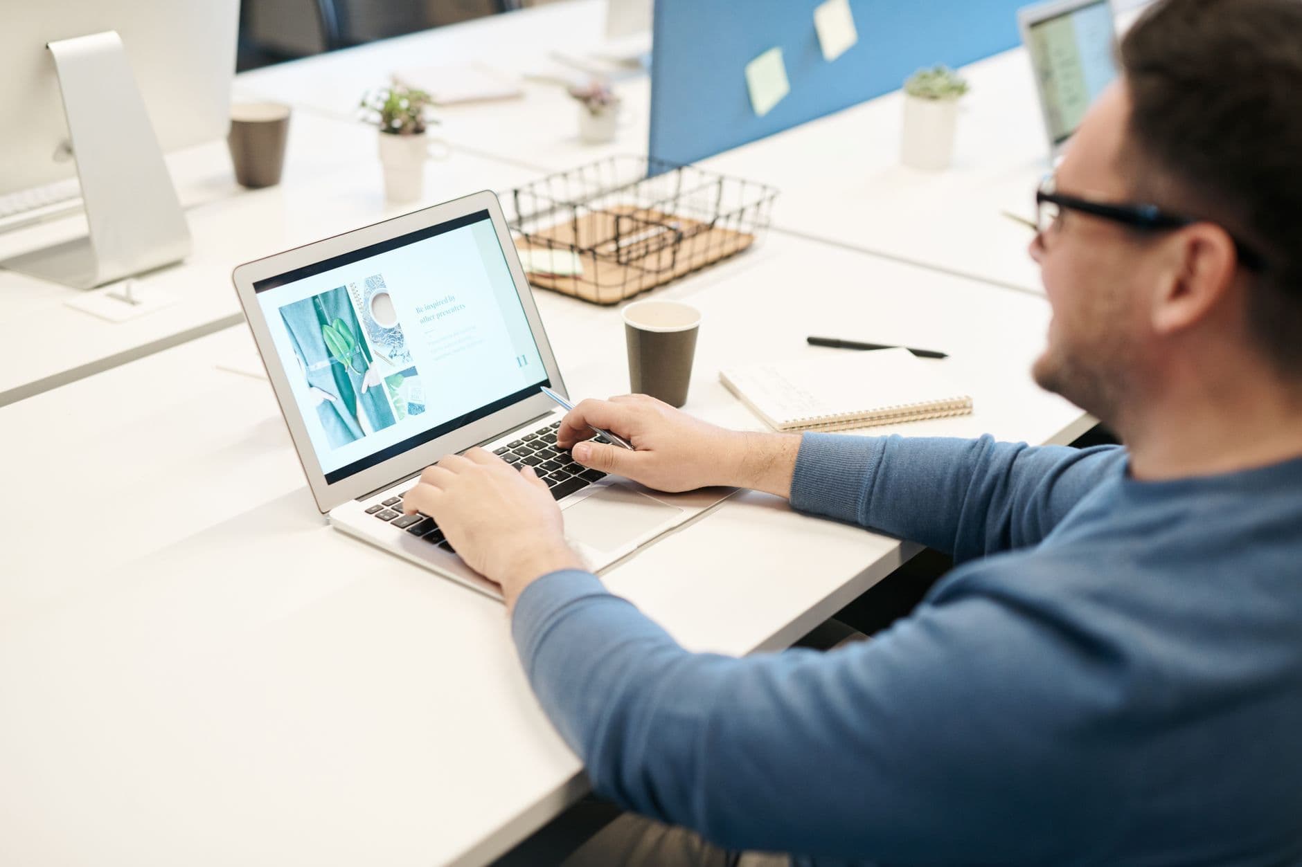 Adult man in office setting working on laptop computer, focused on screen.