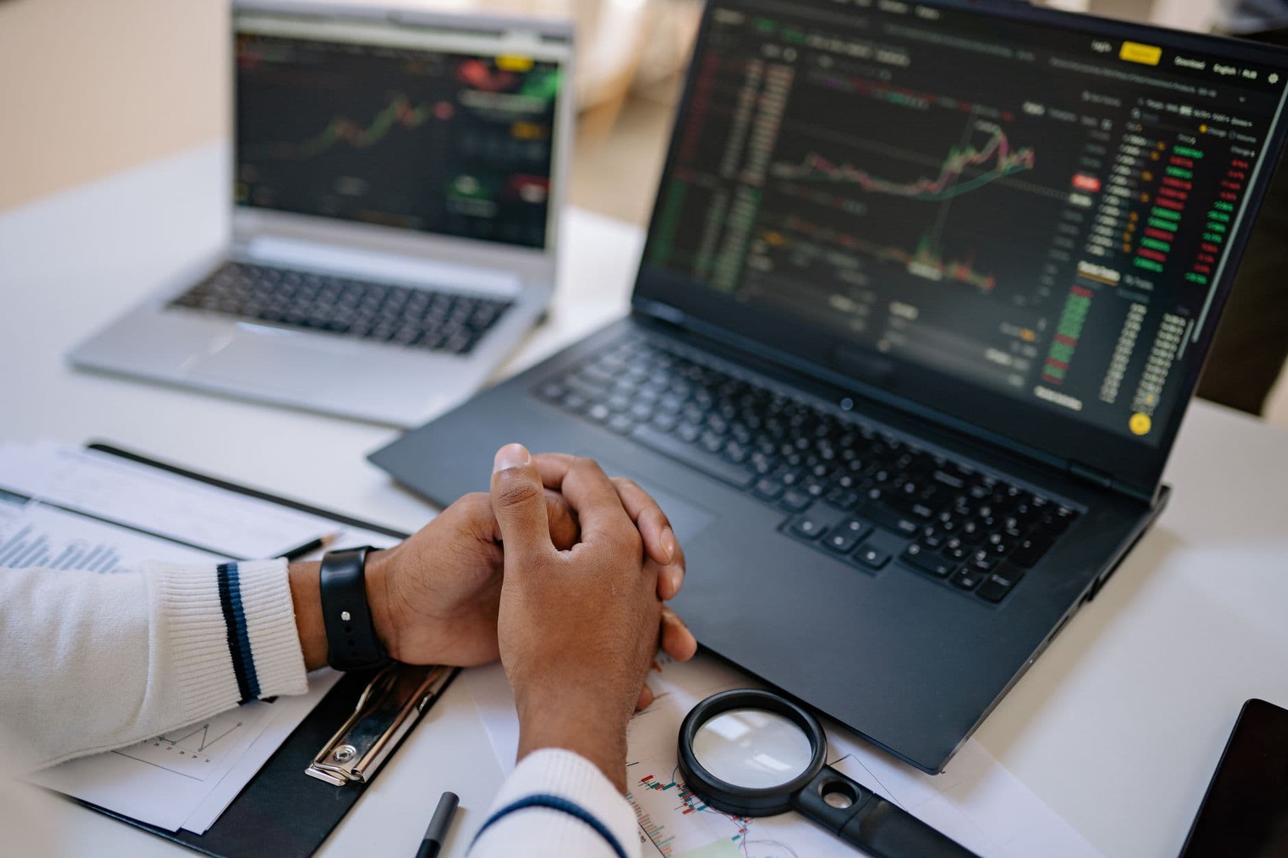 Man seated at a desk using laptops to monitor stock market trends and investments.