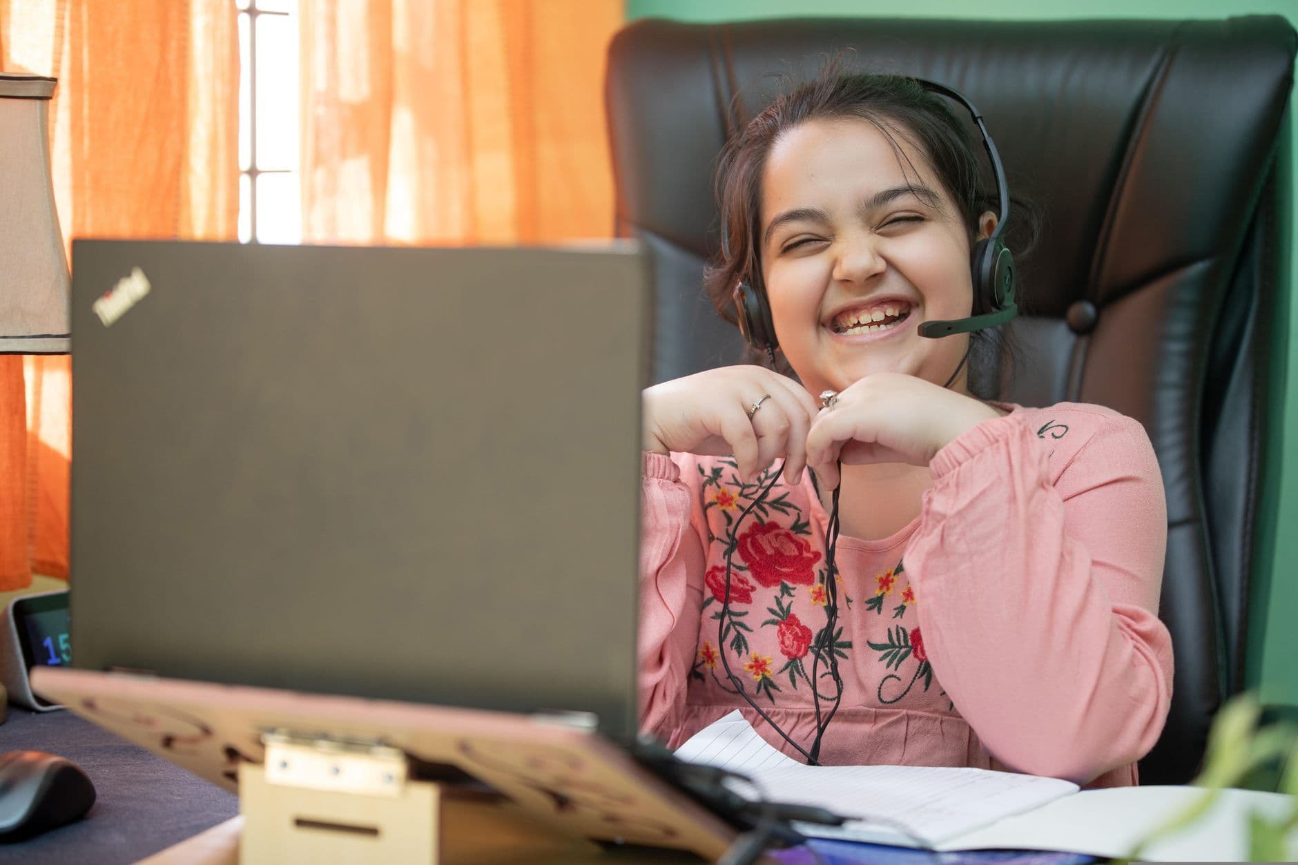 Smiling young girl with headset on a video call, studying online at home.