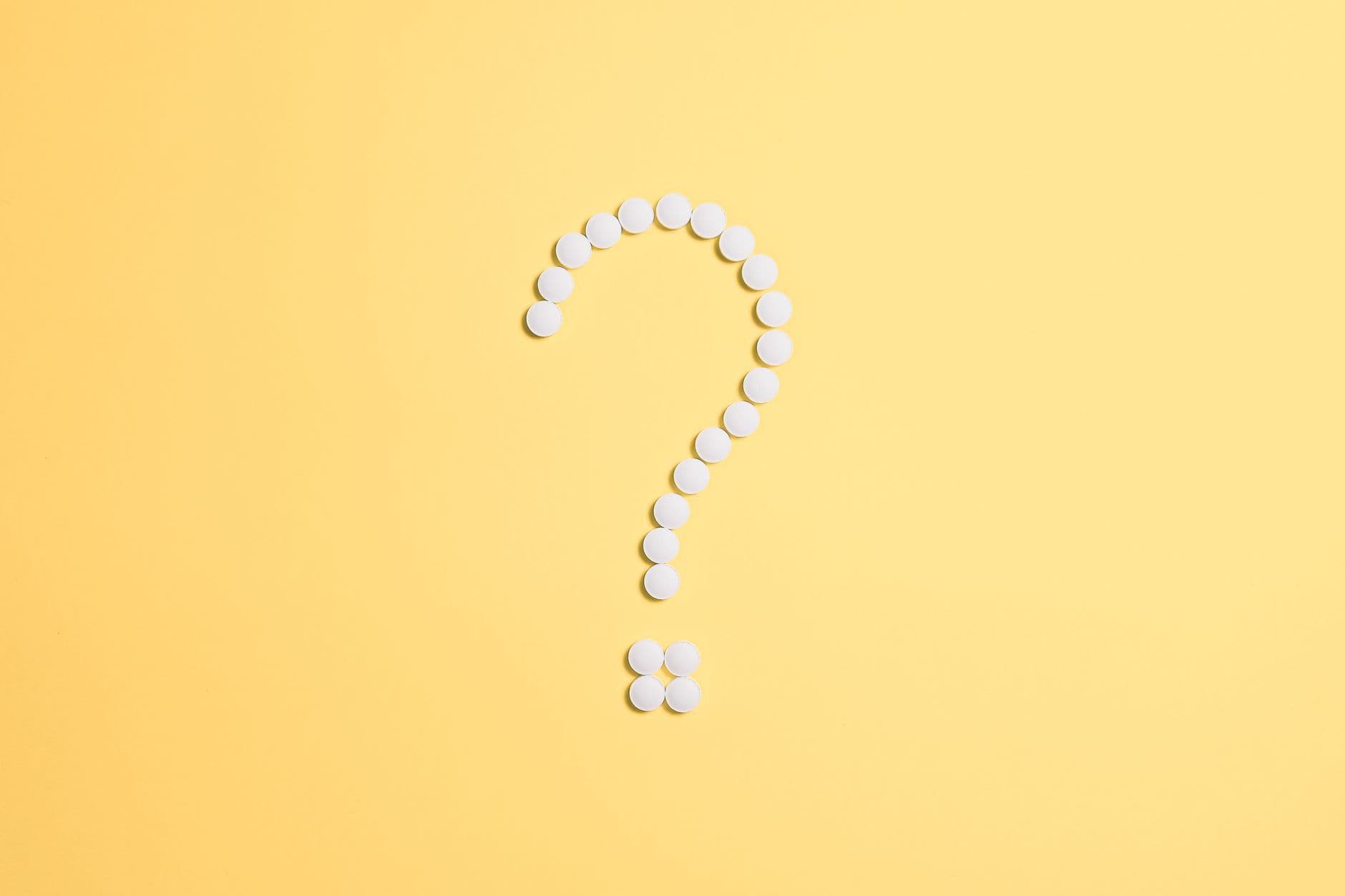 White pills arranged into a question mark shape on a vibrant yellow background.