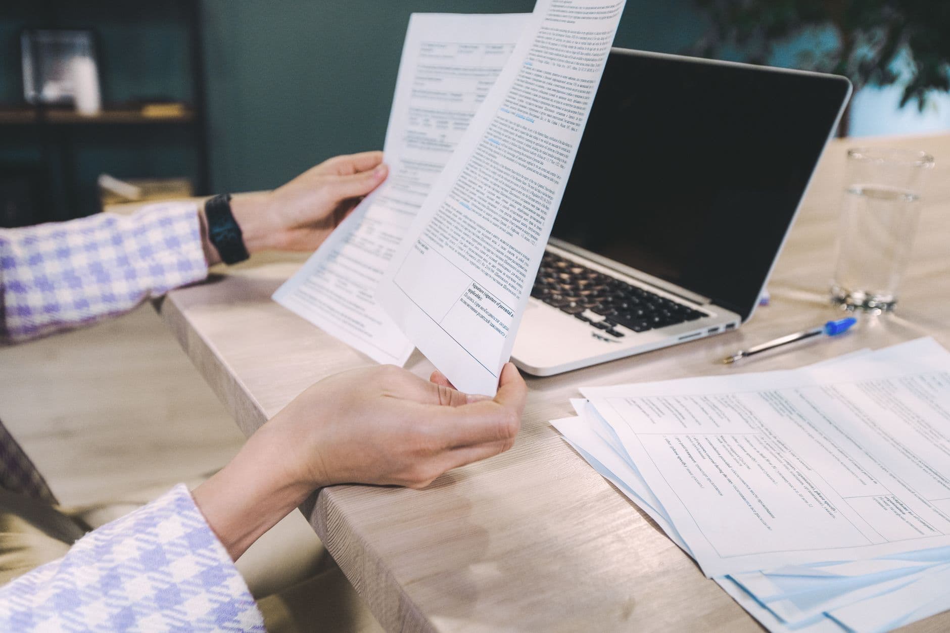 Close-up of hands examining printed documents next to laptop on office desk.